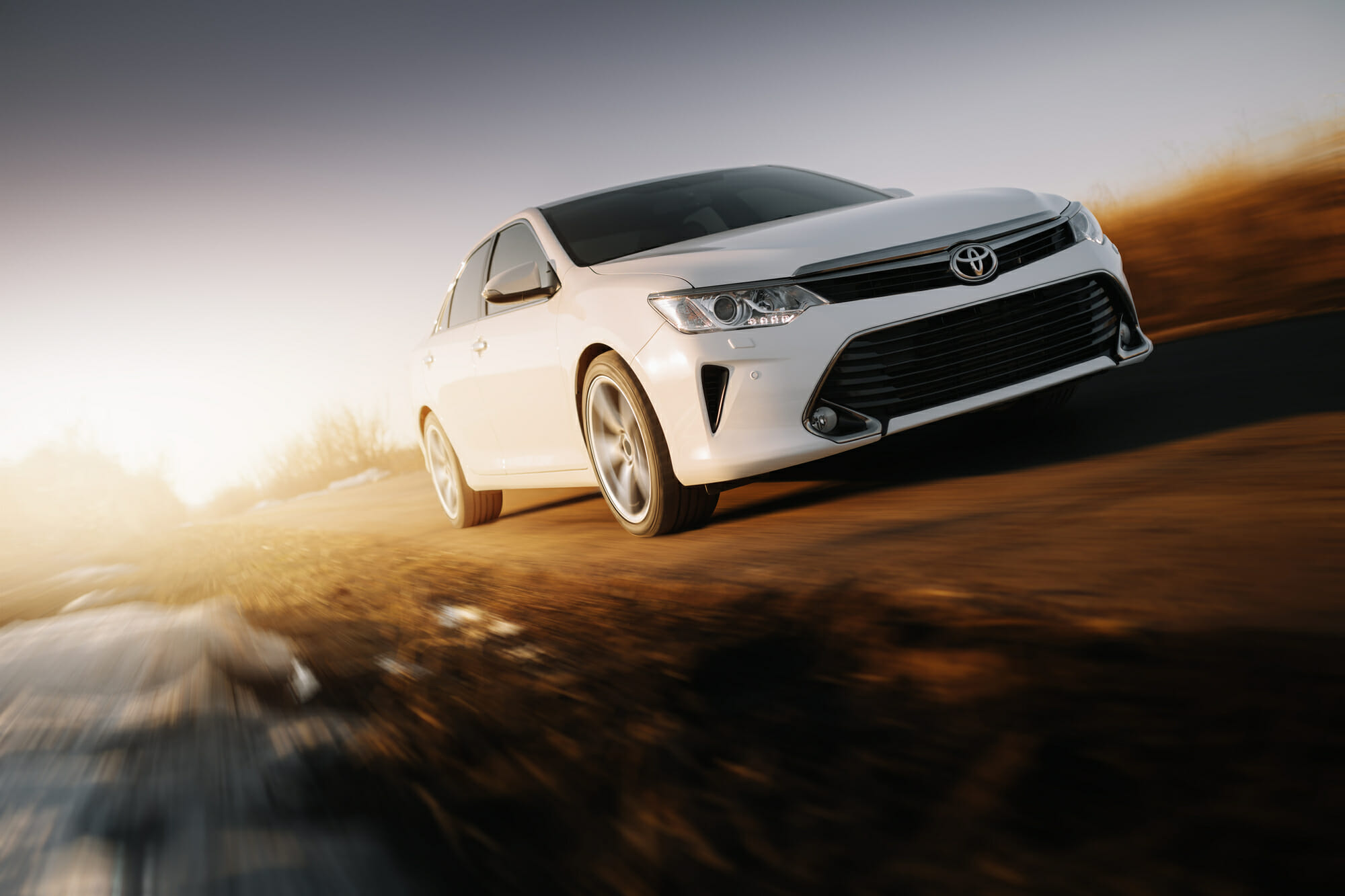 White Toyota Camry in motion with sunrise background